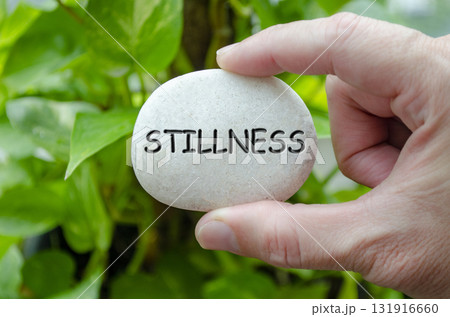 Hand holding a white stone with STILLNESS text engraved on it, representing life purpose of tranquility and peace of mind Hand holding a white stone with STILLNESS text engraved on it, representing life purpose of tranquility and peace of mind 131916660