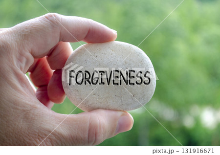Hand holding a white stone with FORGIVENESS text engraved on it, representing life purpose of letting go and spiritual release Hand holding a white stone with FORGIVENESS text engraved on it, representing life purpose of letting go and spiritual release 131916671