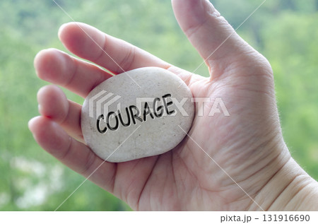 Hand holding a white stone with COURAGE text engraved on it, embodying life purpose of bravery and confidence in challenges 131916690