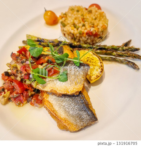 A vibrant dish of crispy-skinned seabass fish fillets served with a vibrant tomato and olive salsa relish, stalks of grilled asparagus and a scoop of rice pilaf topped with a grilled lemon slice A vibrant dish of crispy-skinned seabass fish fillets served with a vibrant tomato and olive salsa relish, stalks of grilled asparagus and a scoop of rice pilaf topped with a grilled lemon slice 131916705