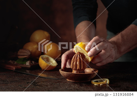 Chef squeezes juice from fresh lemons using an old wooden juicer. Chef squeezes juice from fresh lemons using an old wooden juicer. 131916884