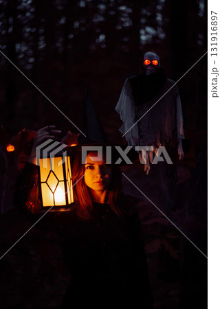 Young beautiful girl in dark forest, ghost behind her. Spooky, mystery atmosphere, witch with lantern in the woods on halloween night. Young beautiful girl in dark forest, ghost behind her. Spooky, mystery atmosphere, witch with lantern in the woods on halloween night. 131916897
