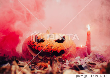 Halloween pumpkin head and glowing candles on autumn foliage. Creepy and scary atmosphere, red smoke on the background 131916918