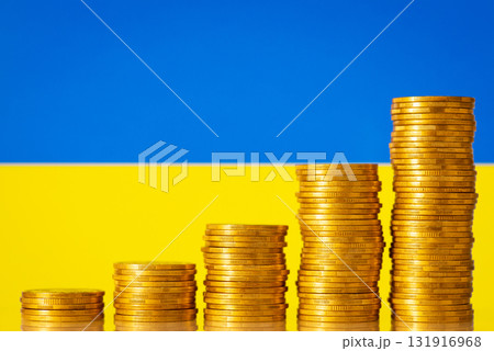 Stacks of golden coins forming upward graph on background of flag of Ukraine. Financial development of Ukraine after the war concept 131916968