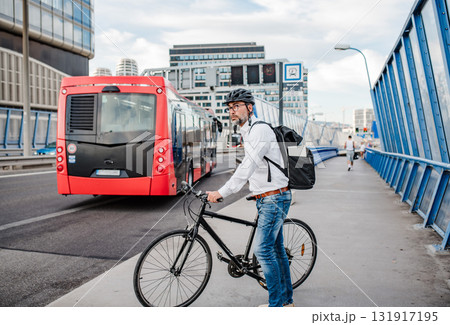 Man riding bike to work in city with helmet and backpack 131917195