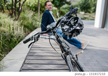 Man sitting in urban park with parked bicycle. 131917210