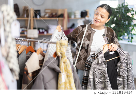Adult woman chooses coat in clothing store Adult woman chooses coat in clothing store 131919414