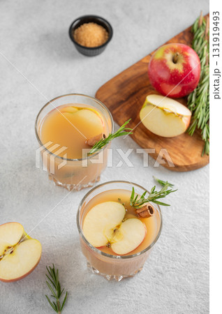 Two glasses of hot apple cider with cinnamon, anise, and rosemary on a light background Two glasses of hot apple cider with cinnamon, anise, and rosemary on a light background 131919493