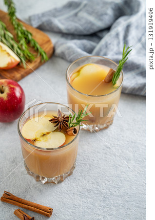 Two glasses of apple cider with cinnamon, anise, and rosemary on a light background with  fruits 131919496