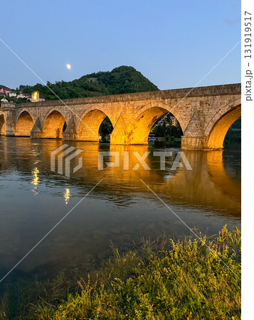 Historic stone bridge with illuminated arches over the Drina River at dusk. Historic stone bridge with illuminated arches over the Drina River at dusk. 131919517