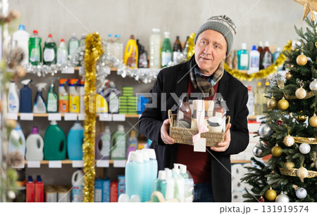 Senior man studies label and choose shower cosmetic present, packaged in basket on Christmas Eve 131919574