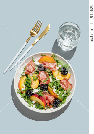 Salad with peaches, arugula, feta, prosciutto and berries in a plate on a blue background 131919629