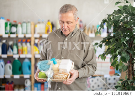 Senior man studies label and choose shower cosmetic present, packaged in basket. 131919667