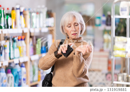 Elderly housewife chooses perfume or aromatic incense in supermarket 131919881