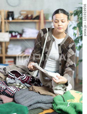 Adult woman chooses sweater in clothing store Adult woman chooses sweater in clothing store 131919956