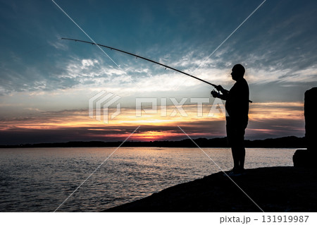 Silhouette Of A Fisherman With His Pole At The Atlantic Coast Of Wales, United Kingdom Silhouette Of A Fisherman With His Pole At The Atlantic Coast Of Wales, United Kingdom 131919987