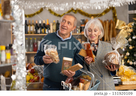 Portrait of elderly couple with sweet products in supermarket - nougat, panettone, marzipan, panellets Portrait of elderly couple with sweet products in supermarket - nougat, panettone, marzipan, panellets 131920109