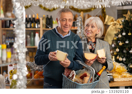 Elderly couple with a basket of groceries buys tasty cheese in grocery store 131920110