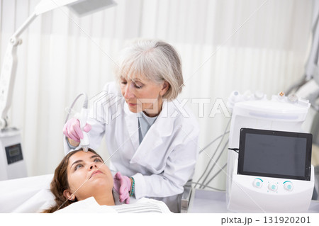 Professional mature female cosmetologist doing needleless high frequency mesotherapy in spa center. Non-invasive skin rejuvenation procedure 131920201