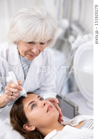 Young woman at appointment with beautician doing ultrasound face cleaning with help of high-frequency ultrasonic waves in cosmetology clinic 131920278