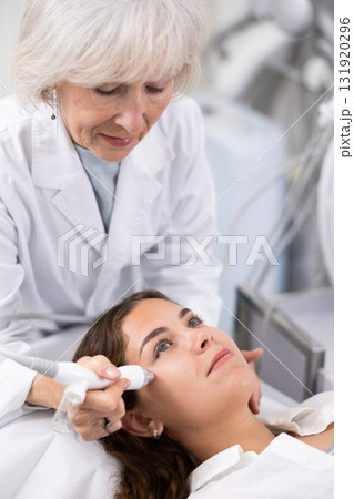 Young woman at appointment with beautician doing ultrasound face cleaning with help of high-frequency ultrasonic waves in cosmetology clinic 131920296