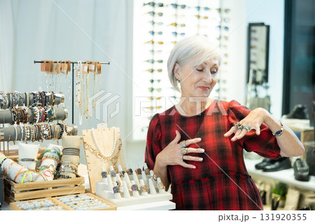 Cheerful elderly woman choosing rings from display with costume jewelry in boutique 131920355