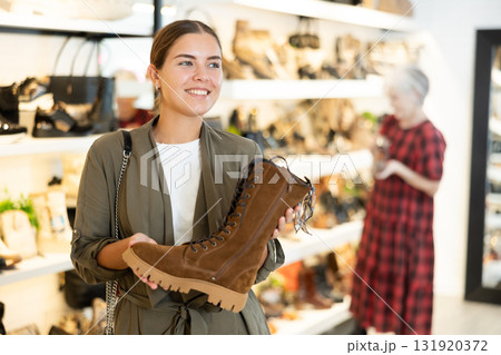 Girl buyer looks at footwear from new collection and picks up new pair of boots for winter. 131920372