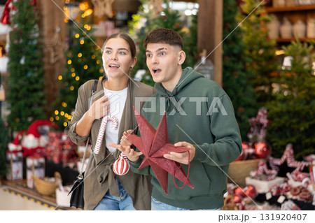 Girl with guy buyer considers New Year and Christmas decorations ornaments for Christmas tree Girl with guy buyer considers New Year and Christmas decorations ornaments for Christmas tree 131920407