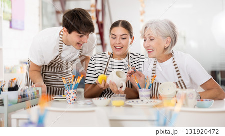 Cheerful older woman with young adult children painting pottery in family workshop Cheerful older woman with young adult children painting pottery in family workshop 131920472