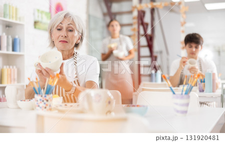 Experienced female artist painting ceramic cup in pottery workshop 131920481
