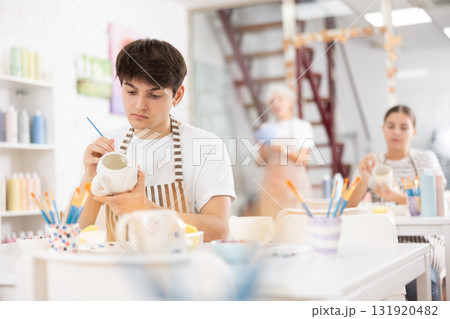 Skilled young artist painting ceramic cup in pottery workshop 131920482