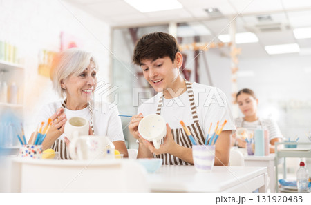 Cheerful guy working with elderly mother in family pottery studio Cheerful guy working with elderly mother in family pottery studio 131920483