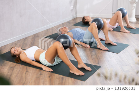 Family grandmother, mother and granddaughter perform fitness exercises lying on floor with softball. Family grandmother, mother and granddaughter perform fitness exercises lying on floor with softball. 131920533