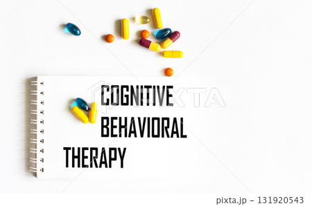 The text "COGNITIVE BEHAVIORAL THERAPY" is written in a notebook next to pills. Medical concept 131920543