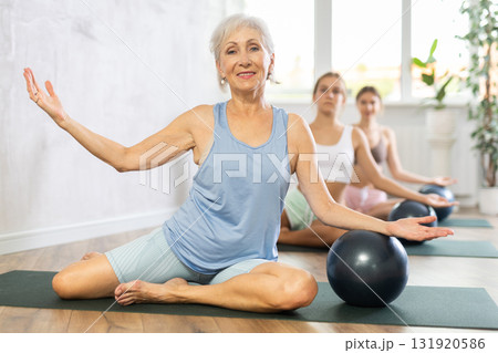 Family grandmother, mother and granddaughter perform fitness exercise sitting on floor with softball 131920586