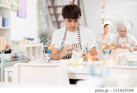 Talented young artisan applying design to ceramic mug in pottery studio 131920599