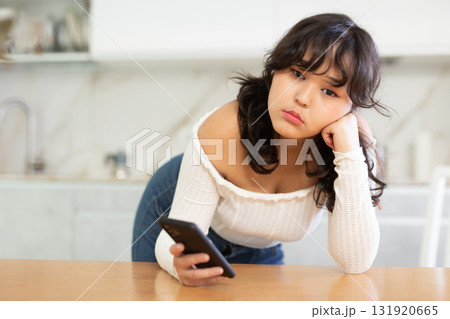 Sad young girl waiting for call from boyfriend in home interior 131920665