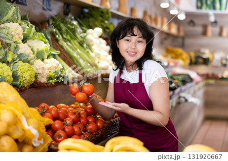 Young asian salesgirl offering ripe tomatoes in greengrocery Young asian salesgirl offering ripe tomatoes in greengrocery 131920667