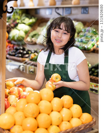 Young saleswoman placing oranges on food stall in grocery store Young saleswoman placing oranges on food stall in grocery store 131920680