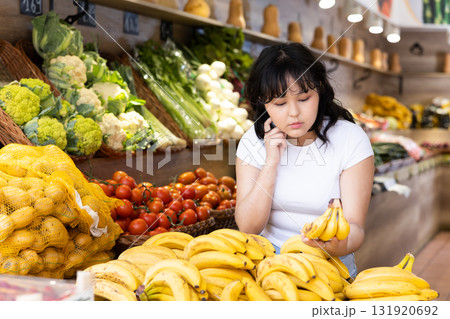 Young girl choosing fresh bananas in fruit and vegetable section of supermarket Young girl choosing fresh bananas in fruit and vegetable section of supermarket 131920692
