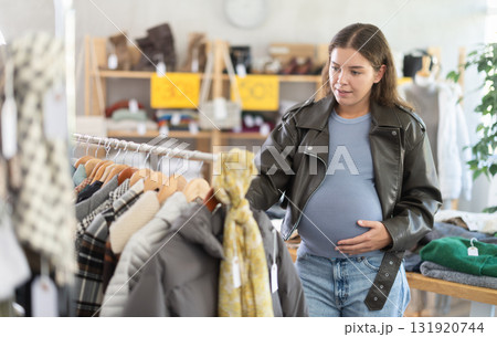 Pregnant woman choosing outerwear in clothing store 131920744
