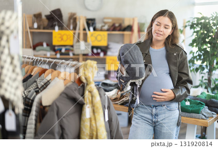 Glad pregnant woman choosing fur hat in clothing store 131920814