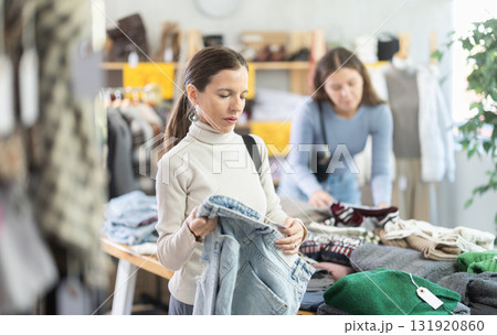Attentive middle-aged woman choosing jean pantaloons in clothing store 131920860