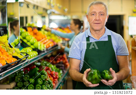 Aged salesman holding peppers at food stall in greengrocery 131921072