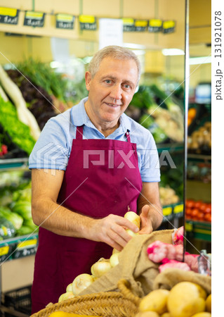 Professional old male seller putting onion on shelves in grocery shop Professional old male seller putting onion on shelves in grocery shop 131921078