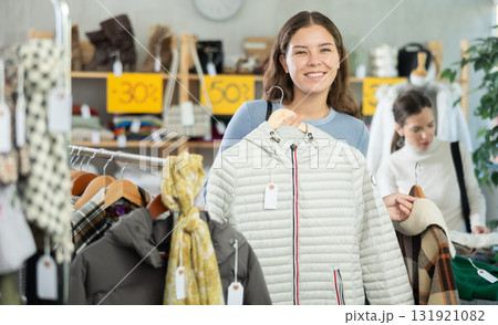 Happy girl chooses fashionable down jacket in clothing store 131921082