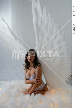 Beauty woman poses topless with angel wings in a dreamy studio setting Beauty woman poses topless with angel wings in a dreamy studio setting 131921145