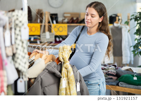 Pregnant woman choosing outerwear in clothing store 131921157