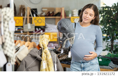 Pregnant woman choosing fur hat in clothing store 131921172