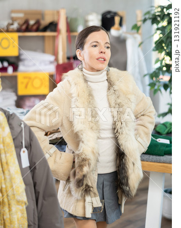 Glad middle-aged woman trying on fur coat in clothing store Glad middle-aged woman trying on fur coat in clothing store 131921192